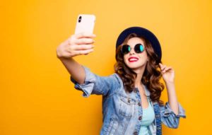 Woman wearing sun glasses taking a selfie over yellow background